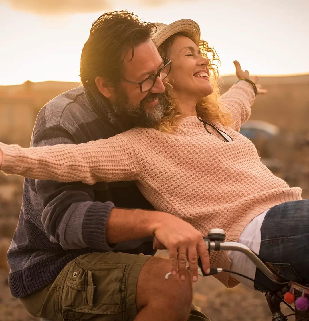 Ett glatt medelålders par som båda cyklar på en cykel i solnedgången